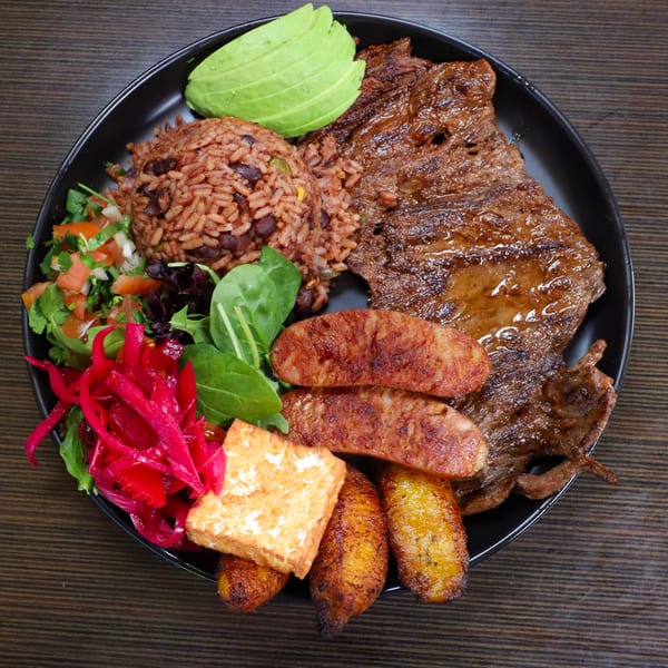 A Lempira Restaurant platter with grilled steak, rice, beans, avocado, plantains, sausage, and salad.