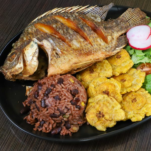 Fried whole fish with rice and beans, fried plantains, and a side salad with radish.
