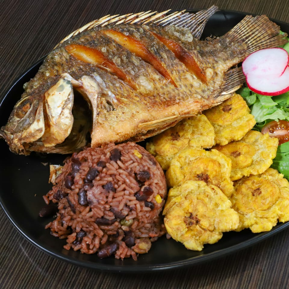 Fried whole fish with rice and beans, fried plantains, and a side salad with radish.