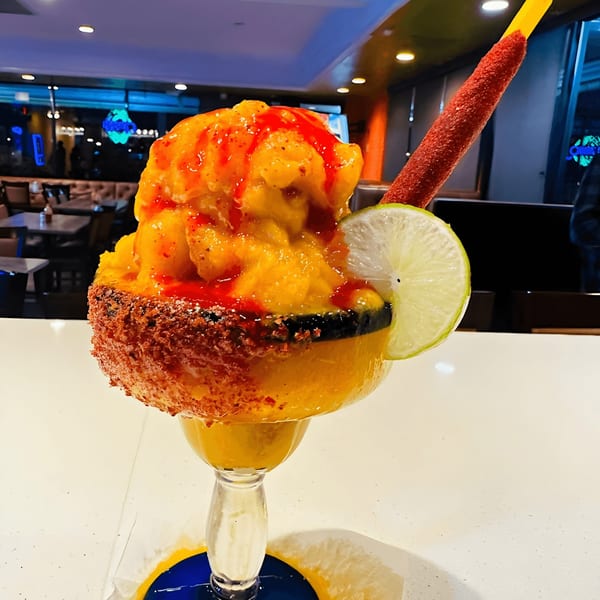 A vibrant mango margarita with chili rim, lime, and a tamarind candy straw at Lempira Restaurant.