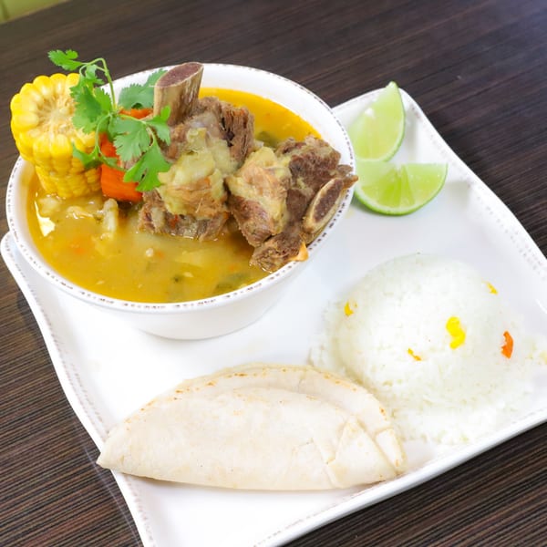 Hearty Latin-American beef rib soup with corn, cilantro, rice, tortillas, and lime wedges.
