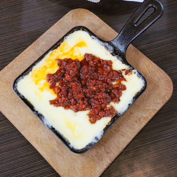 Melted white cheese with a center of red chorizo in a black cast iron pan on a wooden board.